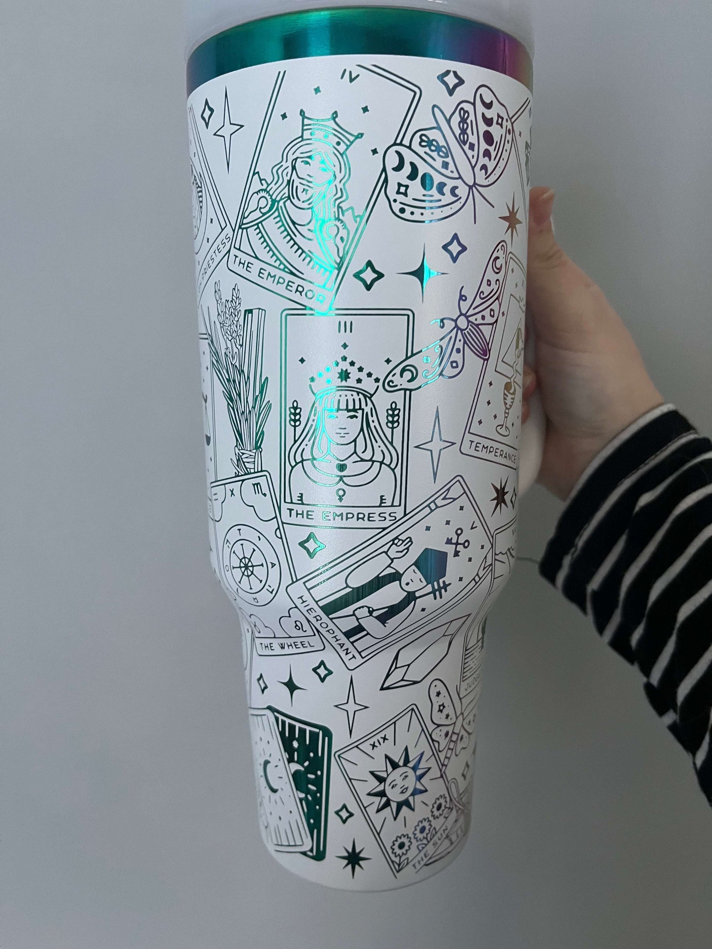 Tumbler with tarot card design held by a hand on a light gray background
