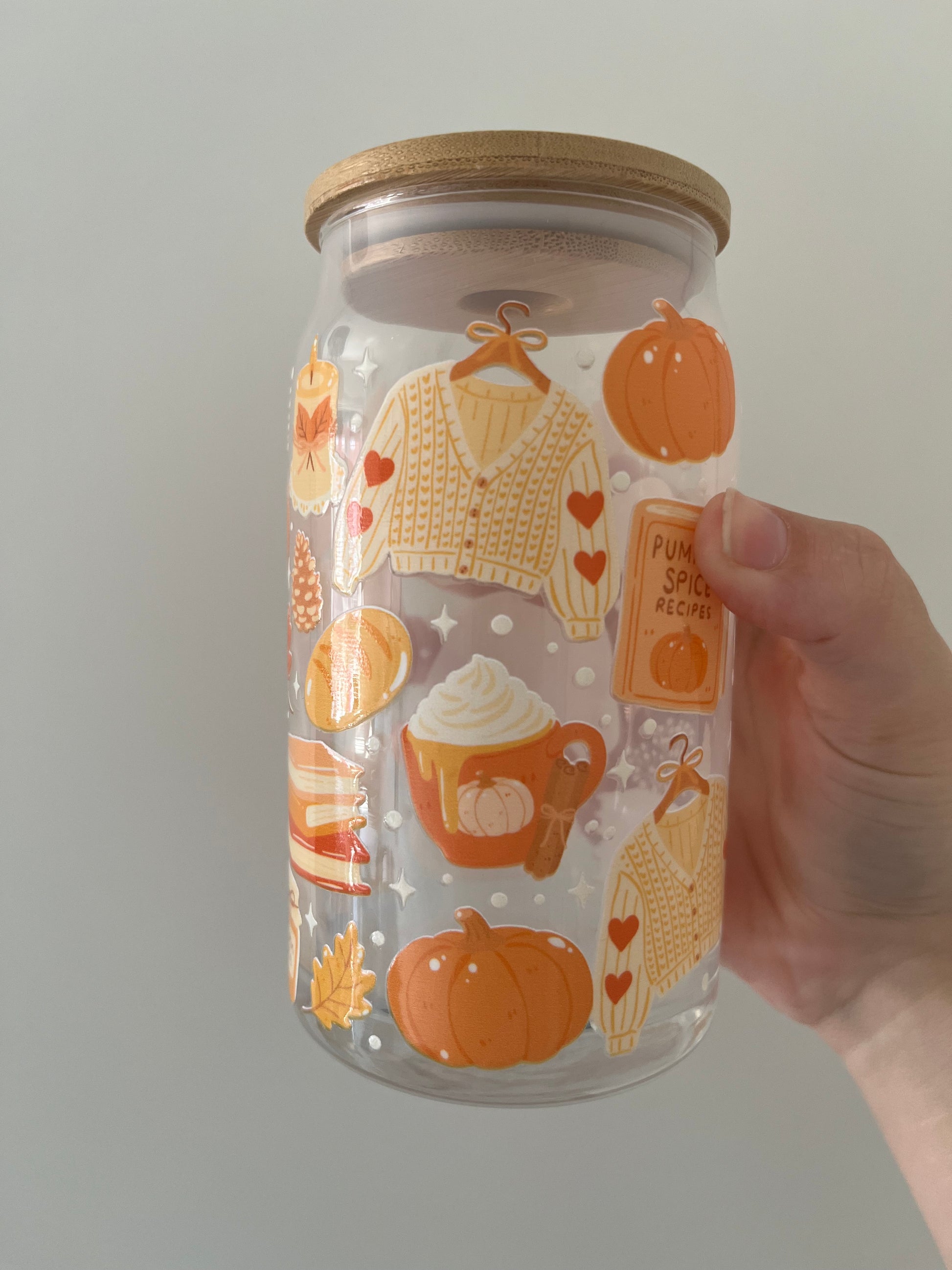 Glass jar with autumn-themed illustrations held by a hand against a neutral background
